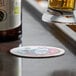 A beer glass being poured over a 4" white round customizable paper coaster.