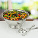 A silver bowl of salad with a pair of Tabletop Classics by Walco stainless steel salad tongs.