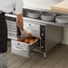 A man using a ServIt freestanding drawer warmer to put food in a drawer.