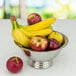 A Tabletop Classics by Walco stainless steel bowl filled with bananas and apples on a white table.