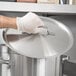 A person wearing white gloves holding a Vollrath stainless steel domed pot lid.