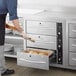 A man using a ServIt triple built-in drawer warmer to put food in a metal container.
