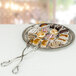 A silver tongs picking up a pastry from a plate of pastries.
