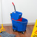 A Rubbermaid blue mop bucket with red wringer and dirty water bucket on the floor.