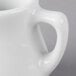 A close-up of a Tuxton white porcelain creamer.