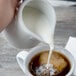 A person pouring milk into a white pitcher.