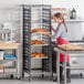 A woman in a red apron using a Cambro sheet pan rack to store bread.