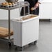 A man pouring brown food into a white Cambro ingredient storage bin.