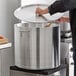 A person using a wooden spoon in a large silver pot with a Choice aluminum pot cover.