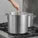 A person stirring a Choice heavy weight aluminum stock pot on a stove.