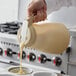 A person pouring batter from a Vollrath Dripcut server into a cupcake tin.