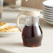 A clear polycarbonate teardrop pitcher of syrup on a table.