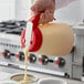 A person using a Vollrath Dripcut server to pour batter into a cupcake tin.