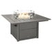 A POLYWOOD slate grey square fire pit table with a glass top over a fire.