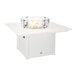 A white square fire pit table with a glass wind guard around the flame area.