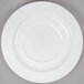 A close-up of an Arcoroc white porcelain saucer with a white rim on a gray surface.