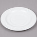 An Arcoroc white porcelain saucer with a small rim on a gray surface.