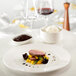 A RAK Porcelain ivory porcelain deep plate with meat and rice on a table with a glass of wine.