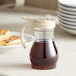 A clear polycarbonate teardrop syrup server filled with syrup on a plate.