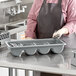 A person in a black apron using a Cambro 4-compartment cutlery box to hold metal utensils.