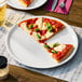 A large ivory porcelain pizza plate holding three slices of pizza, shown on a table setting.