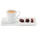 A RAK ivory porcelain coffee cup filled with coffee on a white saucer with chocolates.