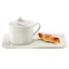 A RAK Porcelain ivory cup filled with foam next to a croissant on a plate.