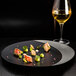 A RAK Porcelain black and silver deep plate with food and a glass of wine on a table in a fine dining restaurant.