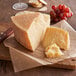 A Piave Vecchio cheese wheel on a cutting board with a knife and grapes.