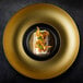 A RAK Porcelain gold and black porcelain plate with food on it.