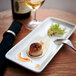 A close-up of a Tuxton eggshell white rectangular tray with scallops holding food on a table.