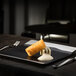 A RAK Porcelain square black and silver plate with food on a table.