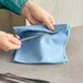 A person using a pair of scissors to cut a Carlisle blue microfiber cloth.