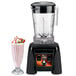 A Waring commercial blender with a pink milkshake in a glass.