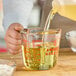 A person pouring liquid into an Anchor Hocking clear glass measuring cup on a kitchen counter.