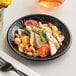A close up of a D&W Fine Pack Black Pearl plastic plate with food and a fork.