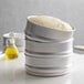 A stack of round metal pans with pizza dough in them.