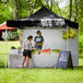 A man and woman standing under a black Backyard Pro canopy selling vegetables.