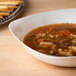 A Fineline ivory plastic bowl filled with soup on a table.