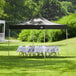 A black Backyard Pro canopy set up with a white table and chairs on grass.