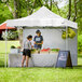 A man and woman standing in a white Backyard Pro tent selling a bunch of vegetables.