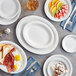 A table set with Acopa Bright White narrow rim stoneware plates, forks, and knives with a slice of pie on a plate.