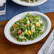 An Acopa narrow rim oval stoneware platter with a salad of arugula, tomatoes, and feta cheese.