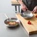 A person cooks meat and vegetables in Vigor stainless steel frying pans.