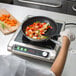 A woman using Vigor SS1 Series stainless steel frying pans to cook vegetables on a stove.