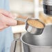 A person using a Tablecraft stainless steel measuring cup to pour brown sugar.