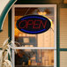 An oval LED open sign with lights on a window.