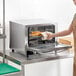 A woman in an apron using a Galaxy countertop convection oven to cook food.