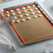 A person using a Mercer Culinary orange silicone baking mat to bake cookies on a baking sheet.