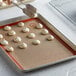 A person using tongs to lift cookies off a Mercer Culinary orange silicone baking mat on a tray.